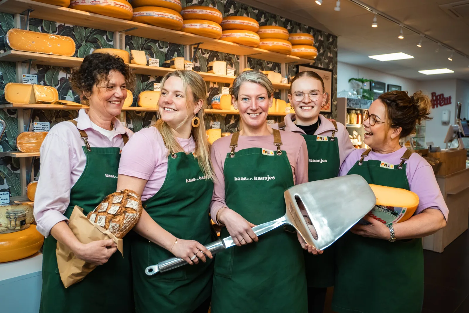 Het team van Kaas & Kaasjes in de winkel, met schorten en een grote kaasschaaf
