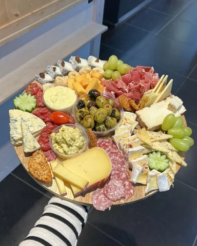Borrelplank voor 6 personen: grote ronde plank met kazen, vleeswaren, dips, olijven, druiven en crackers